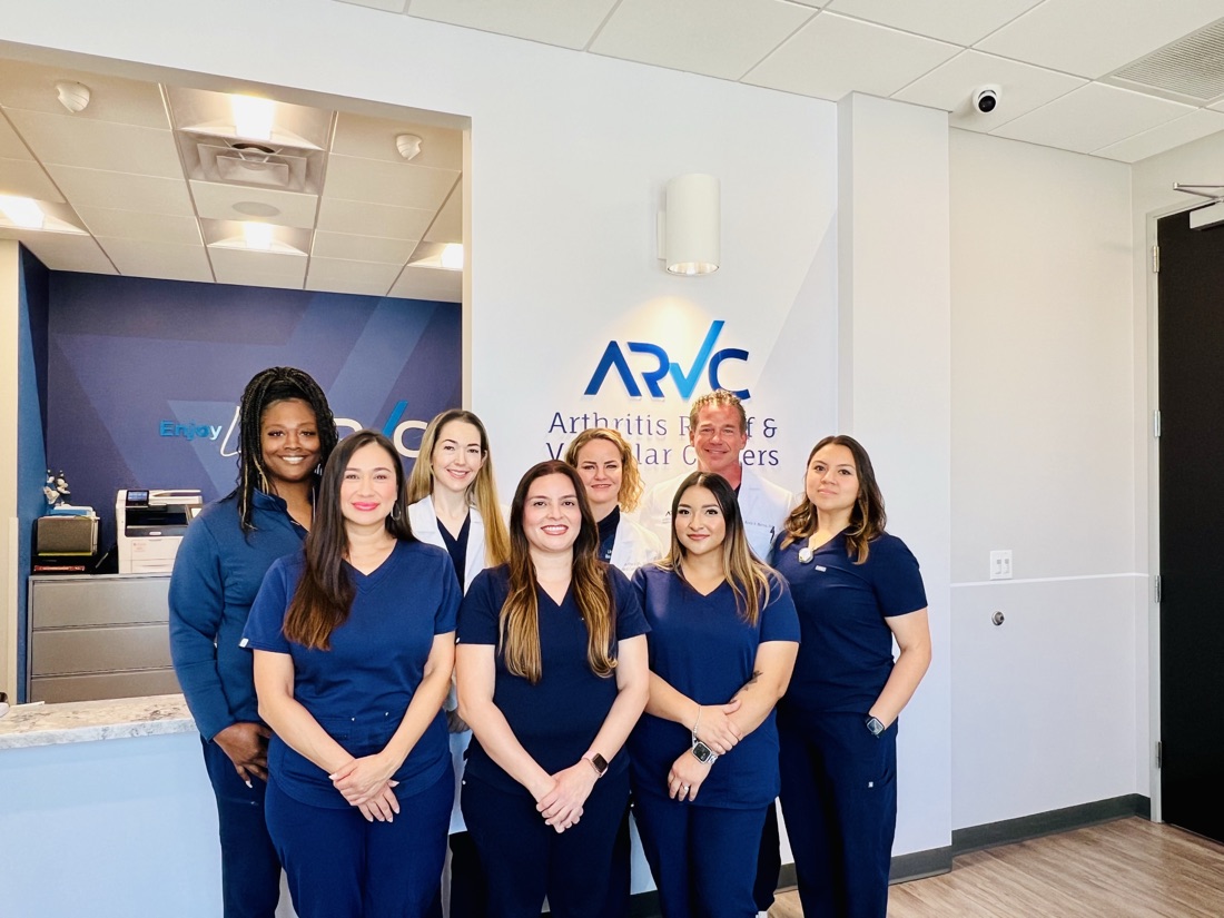The ARV Centers clinical and front-desk team &mdash; eight staff in navy scrubs and white coats &mdash; standing together beneath the ARVC sign at the front desk